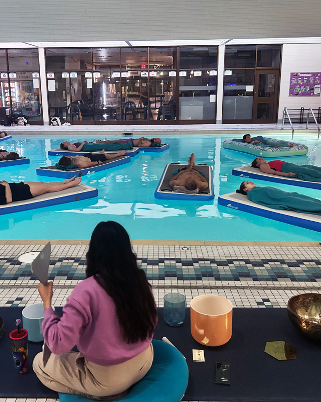 People float in the teach pool on mats while a facilitator makes soothing sounds from sound bowls. 