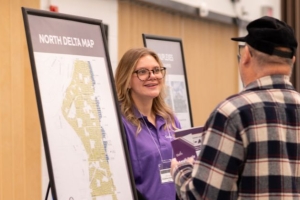 Delta staff member standing next to a map of North Delta and speaking with a member of the public at the PLAN-A-THON event.